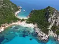 Malownicze **Korfu plaże** w zatoce, z turkusową wodą, zielonymi wzgórzami i tłumem plażowiczów.