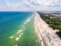 Słoneczny dzień na plaży w Sarbinowie nad morzem. Tłumy turystów odpoczywają na piasku, kąpią się w morzu i spacerują wzdłuż brzegu.