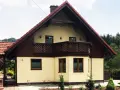 Jasny dom z drewnianymi elementami i balkonem, otoczony zielenią. Może to być dom Adama Małysza w Wiśle.