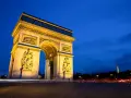Łuk Triumfalny nocą, z widoczną w oddali Wieżą Eiffla. Światła samochodów tworzą smugi na tle **Champs-Élysées**.