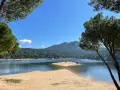 Piękna, piaszczysta plaża nad jeziorem w pobliżu Madrytu, otoczona sosnowym lasem i górami.