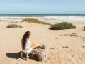 Kobieta pije herbatę na piaszczystych plażach Tunezji, z widokiem na ocean.