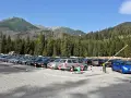 Parking przy wejściu na Morskie Oko. Rząd samochodów pod górskimi szczytami i gęstym lasem.