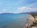 Słoneczny dzień na plaży Kalamaki. Ludzie pływają, opalają się i relaksują na piasku. Woda jest spokojna i turkusowa.