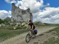 Młody rowerzysta przemierza malownicze **Jura Krakowsko-Częstochowska szlaki**, mijając ruiny zamku na tle błękitnego, chmurnego nieba.