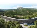 Nowy hotel w górach, o futurystycznym, zakrzywionym kształcie, otoczony gęstym lasem iglastym. W tle widać łagodne, zalesione wzgórza.