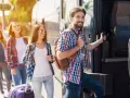 Grupa młodych ludzi z plecakami i walizką wsiada do autobusu, gotowa na wycieczki fakultatywne.