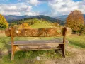 Drewniana ławka z napisem "Ciechocinek" na tle jesiennych gór i zielonych wzgórz. Widok na Beskid Sądecki.