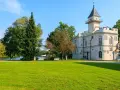 Biały pałac z wieżą, otoczony zielenią, nad jeziorem. Jeden z urokliwych zamków na Mazowszu.
