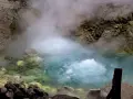 Gorący, bulgoczący onsen otoczony skalistym, parującym krajobrazem. Woda ma turkusowy odcień, a brzegi pokryte są żółtymi osadami.