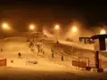Oświetlony nocą stok narciarski Gołębiewski, z armatkami śnieżnymi i narciarzami.