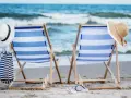 Dwa leżaki na plaży, gotowe na idealny weekend nad morzem. W tle fale, a obok kapelusze i torba plażowa.