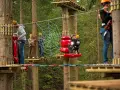 Park linowy Base Camp Istebna: ludzie na platformach wśród drzew, pokonują przeszkody, w tym pajęczynę.