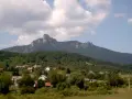 Widok na malowniczą wieś u podnóża góry Klek. Domy z czerwonymi dachami wtulone w zieleń, a nad nimi majestatyczny, skalisty szczyt.
