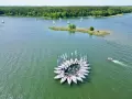 Żaglówki tworzą okrąg na spokojnym **lago**, otoczone zielonym lasem.