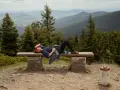 Kobieta odpoczywa na ławce z widokiem na góry. To chyba najładniejszy szlak na Śnieżnik, idealne miejsce na chwilę relaksu.