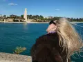 Kobieta z blond włosami podziwia pomnik w Brindisi. W tle błękitne morze i błękitne niebo.
