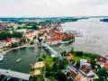 Malownicze miasta na Mazurach z widokiem na jezioro i liczne łodzie. Biały most łączy brzegi, a czerwone dachy domów tworzą urokliwy krajobraz.