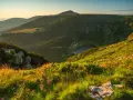Słoneczny poranek w Karkonoszach. Widok na górzyste tereny, lasy, jezioro i charakterystyczny szczyt.