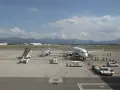 Samolot Ryanair na płycie lotniska Bergamo. W tle góry, na pierwszym planie schody, pojazdy obsługi naziemnej i pasażerowie.