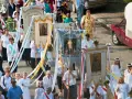 Procesja z banerami religijnymi, w tym z napisem "Boże Ciało 26". Ludzie niosą obrazy i kwiaty.