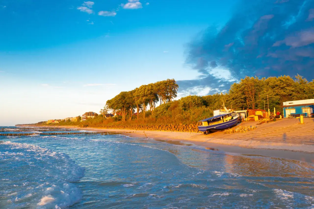Zachód słońca nad morzem, idealny na zwiedzanie Ustronia i okolic. Piękna plaża, falochrony i łódź na piasku.