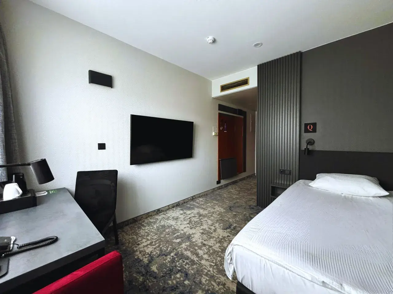 Pokój w hotelu Qubus Gorzów: łóżko, biurko, TV i drzwi do łazienki.