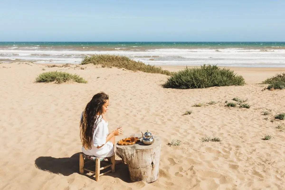 Kobieta pije herbatę na piaszczystych plażach Tunezji, z widokiem na ocean.