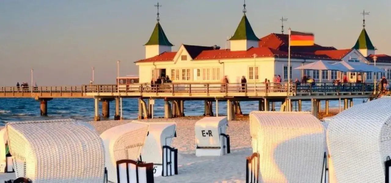 Plaża z koszami i molo, gdzie widać budynek restauracji i niemiecką flagę. Atrakcje po niemieckiej stronie Świnoujścia zachęcają do spacerów.