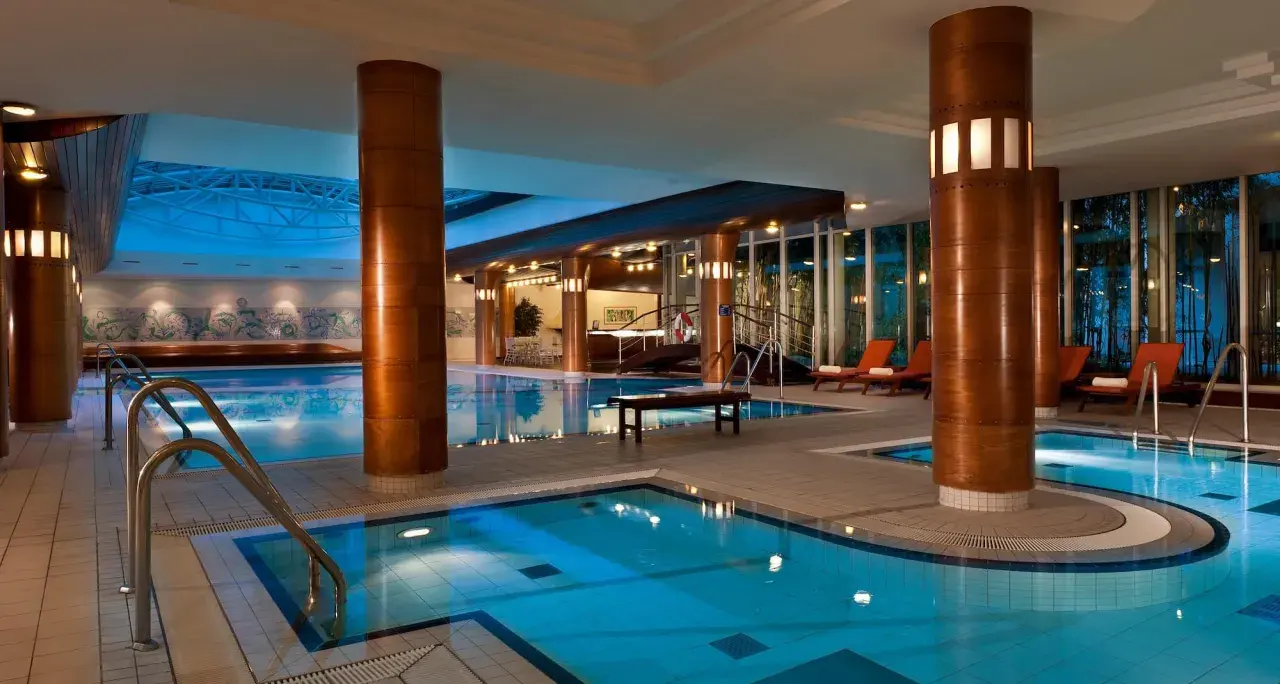 Basen hotelowy Radisson Blu Radebeul z niebieską wodą, drewnianymi kolumnami i leżakami.