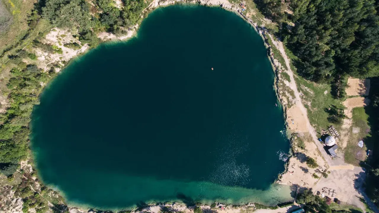 Serce polskiego balatonu, turkusowa woda, otoczona zielenią i piaszczystymi plażami. W oddali widać małą łódkę.