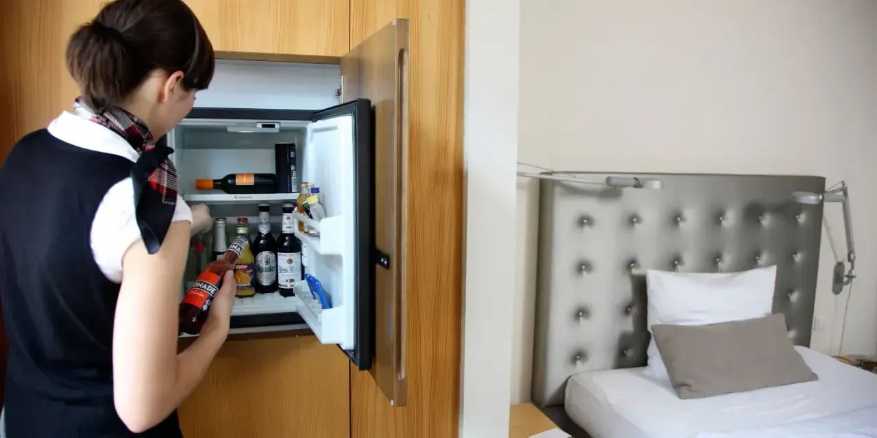 Kobieta sprawdza zawartość minibaru w hotelu. Czy minibar w hotelu jest płatny? Widać butelki z napojami i wino.