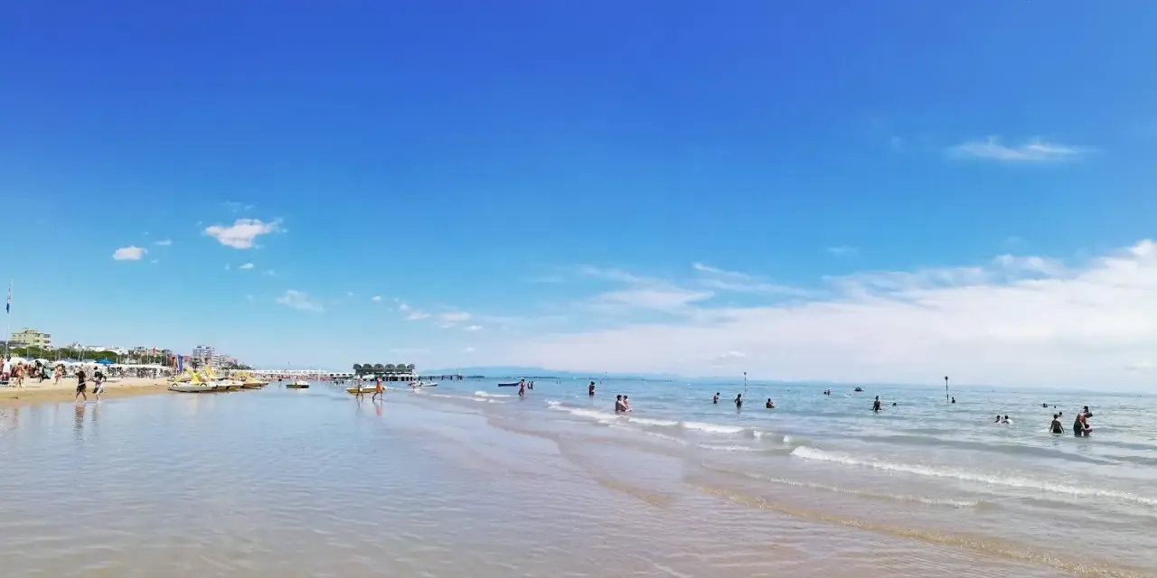 Słoneczna triest plaża piaszczysta z turkusową wodą i błękitnym niebem. Ludzie kąpią się i relaksują.