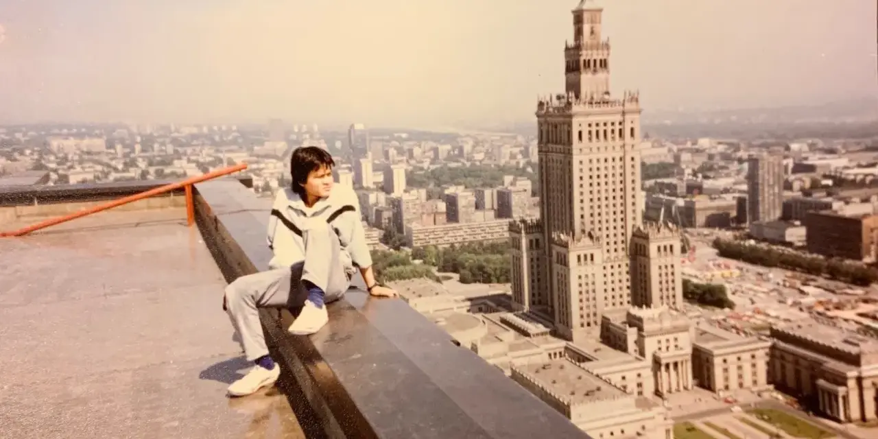 Młody mężczyzna siedzi na dachu, patrząc na panoramę Warszawy. W tle Pałac Kultury i Nauki, który wtedy był najwyższym budynkiem, zanim powstał Marriott.