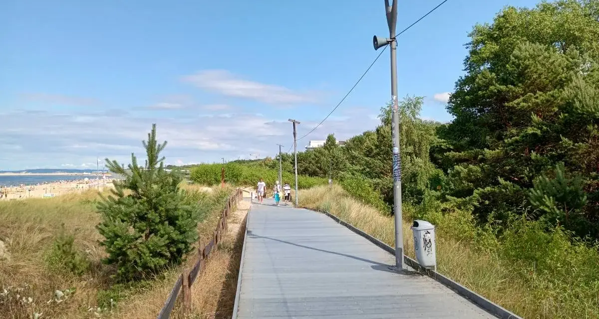 Spacer po promenadzie w Świnoujściu. Widok na plażę, morze i zielone drzewa. Atrakcje dla spacerowiczów.