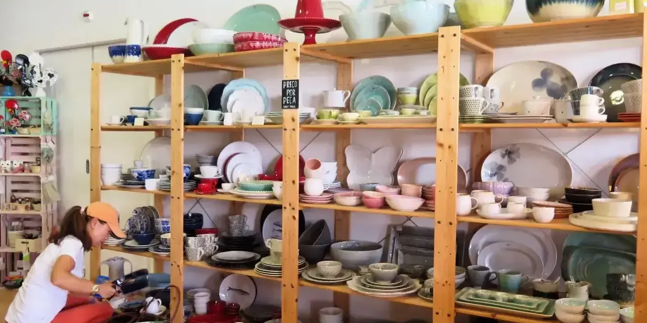 Kobieta wybiera ceramiczne naczynia, idealne pamiątki, które warto co przywieźć z Portugalii. Kolorowe talerze, miski i filiżanki na drewnianych półkach.