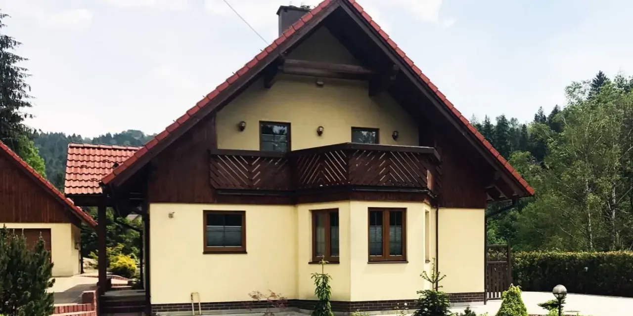 Jasny dom z drewnianymi elementami i balkonem, otoczony zielenią. Może to być dom Adama Małysza w Wiśle.