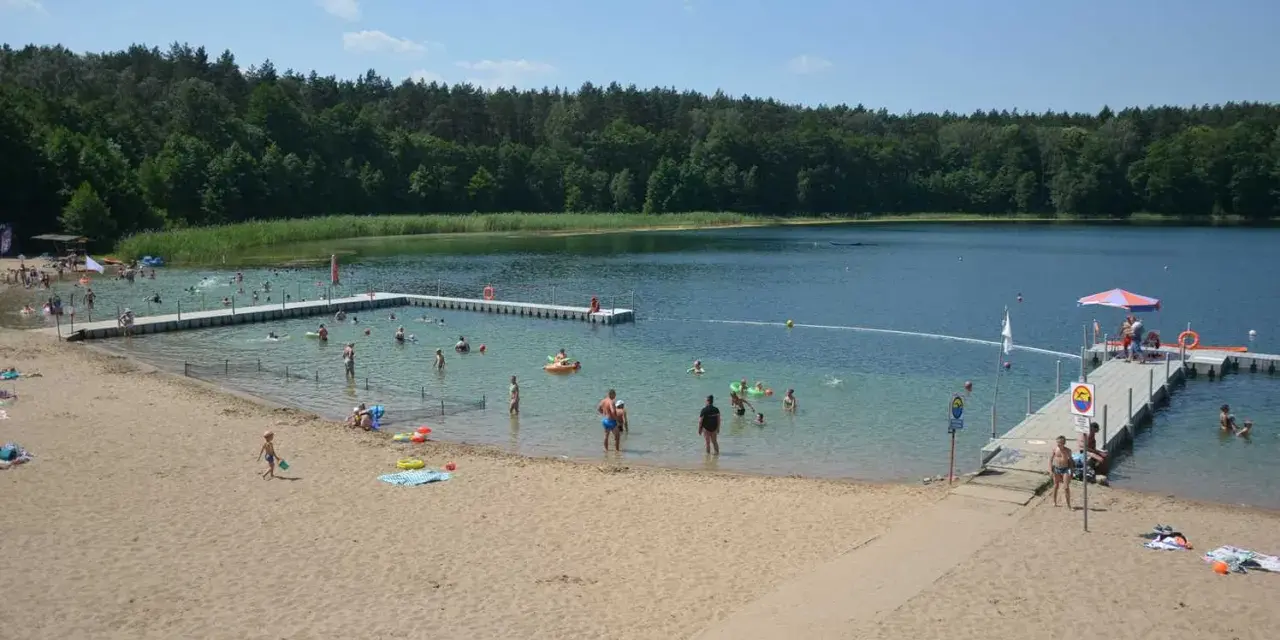 Słoneczny dzień nad jeziorem płotki. Ludzie kąpią się, pływają na dmuchanych zabawkach i odpoczywają na piaszczystej plaży.