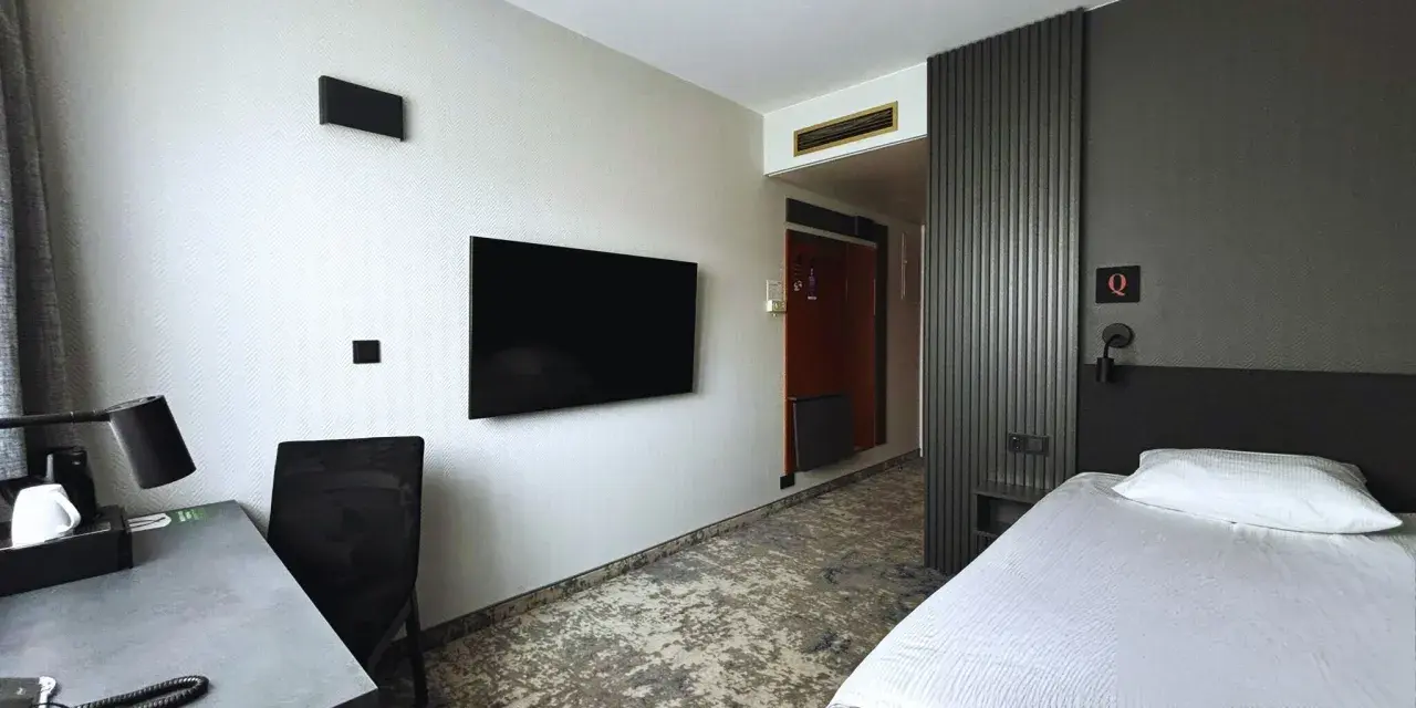 Pokój w hotelu Qubus Gorzów: łóżko, biurko, TV i drzwi do łazienki.