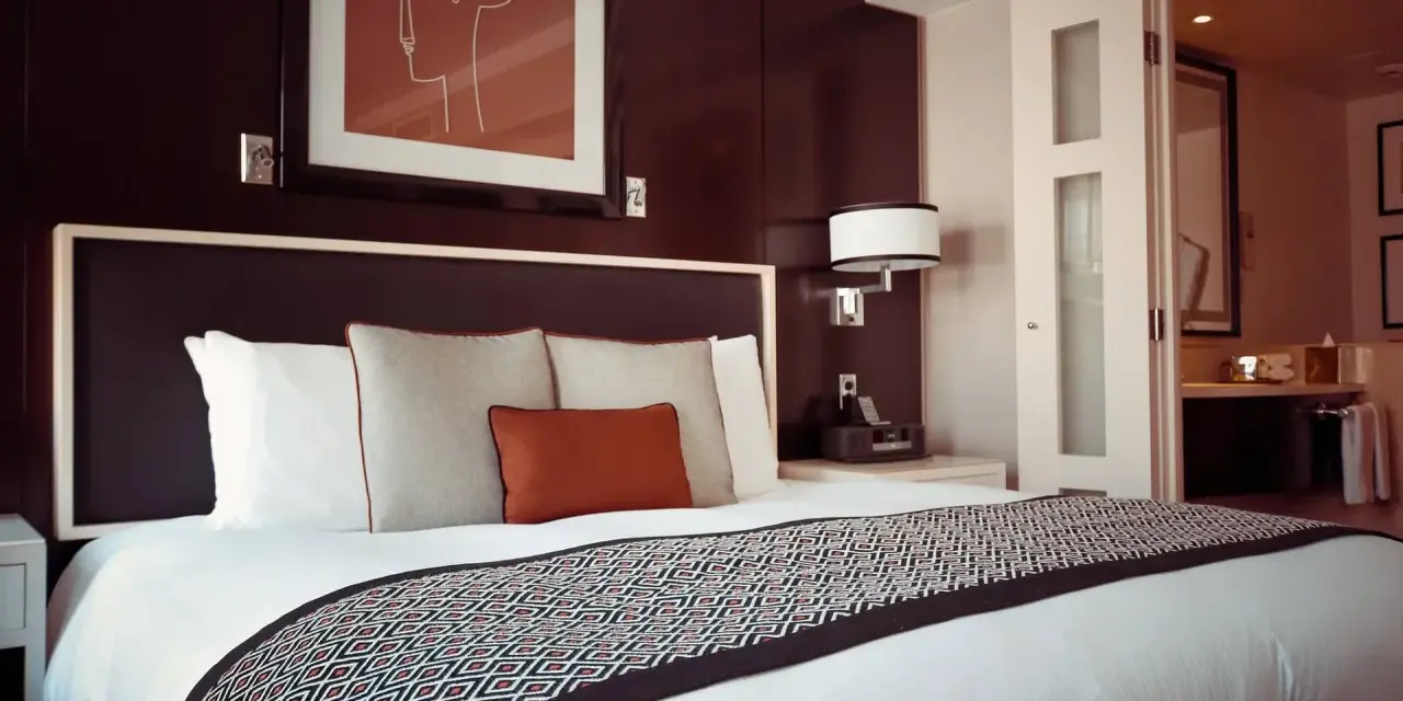 Przytulne łóżko w pokoju hotelowym, gdzie można odpocząć po podróży. To miejsce, gdzie nocleg jest komfortowy i przystępny cenowo, jak w dobrym hostelu.