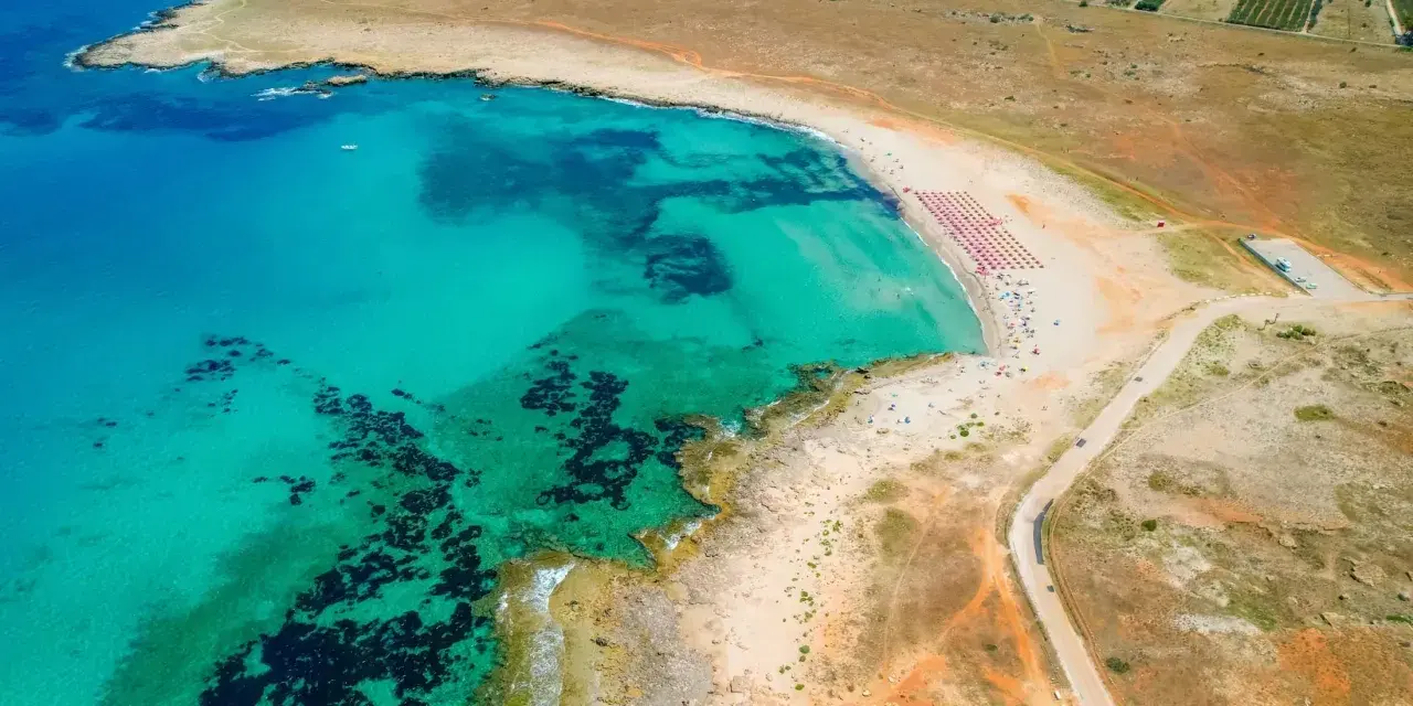 Widok z lotu ptaka na turkusowe morze i piaszczyste bari plaże z rzędami parasoli.