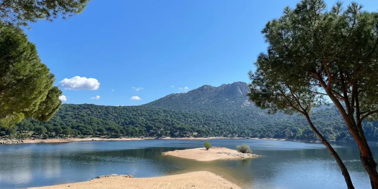 Piękna, piaszczysta plaża nad jeziorem w pobliżu Madrytu, otoczona sosnowym lasem i górami.