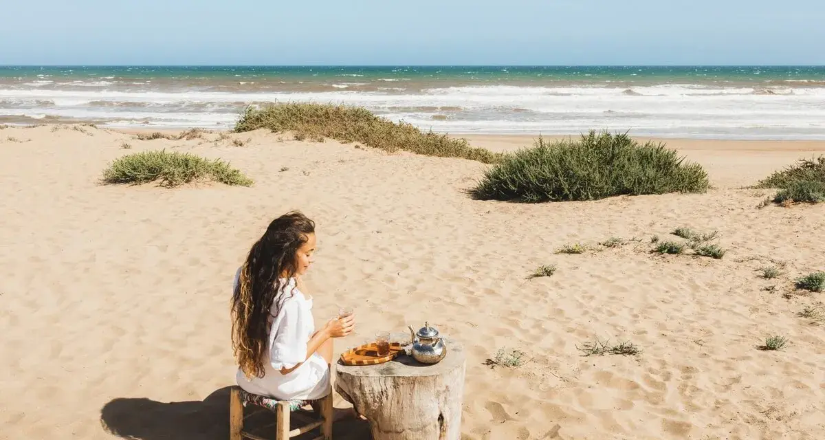 Kobieta pije herbatę na piaszczystych plażach Tunezji, z widokiem na ocean.