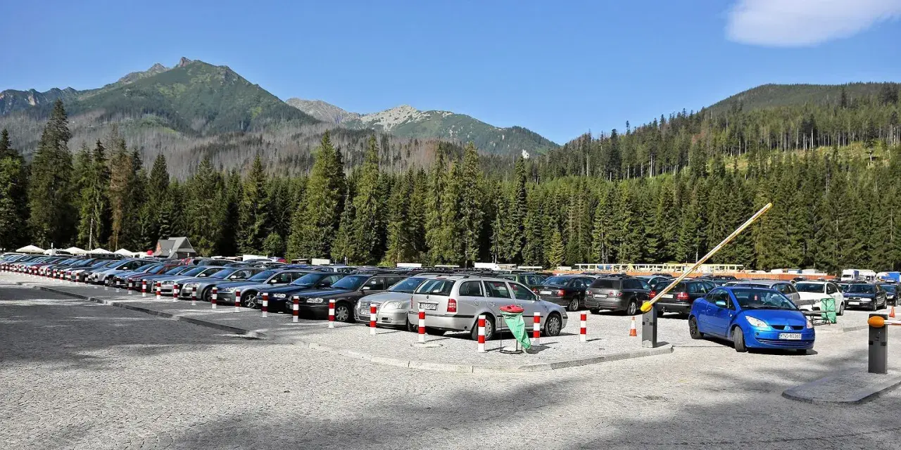 Parking przy wejściu na Morskie Oko. Rząd samochodów pod górskimi szczytami i gęstym lasem.