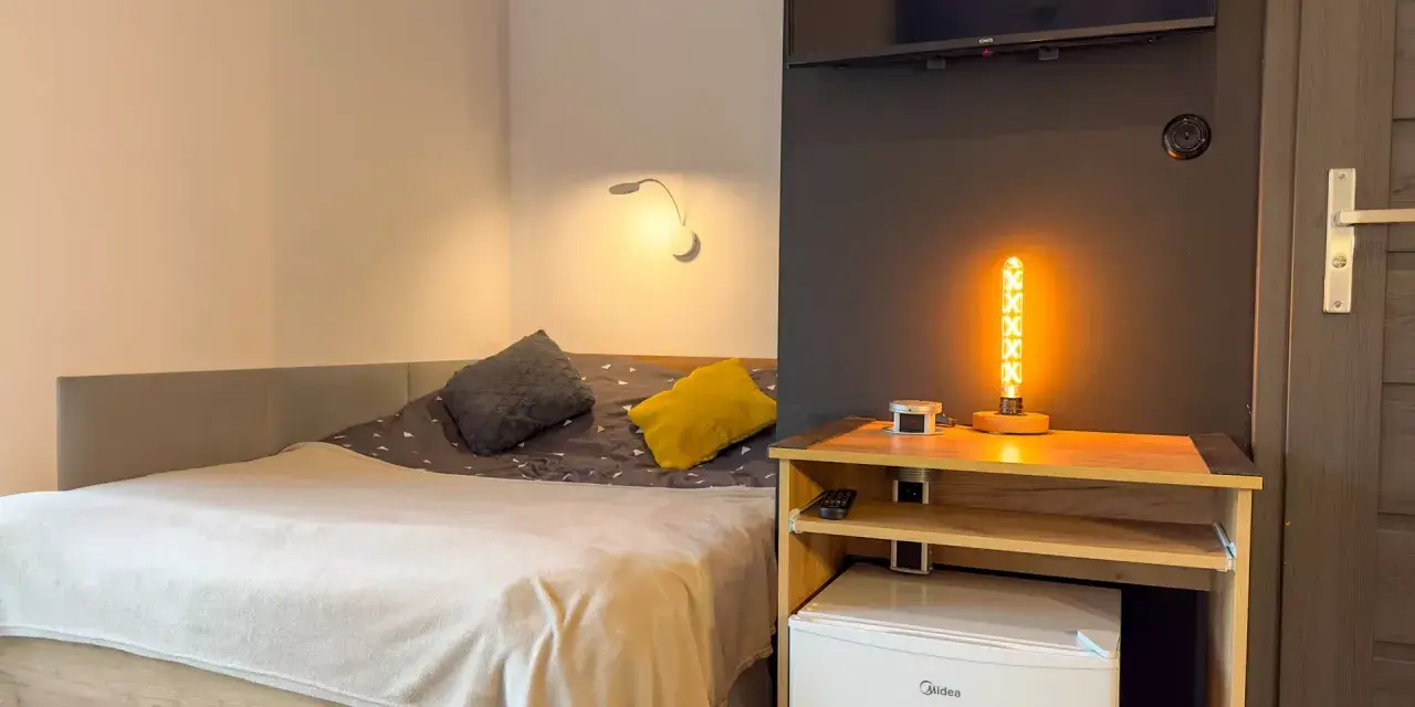 Przytulny pokój z łóżkiem, ozdobną lampą i lodówką. Idealne miejsce na **weekend w Karpaczu**.
