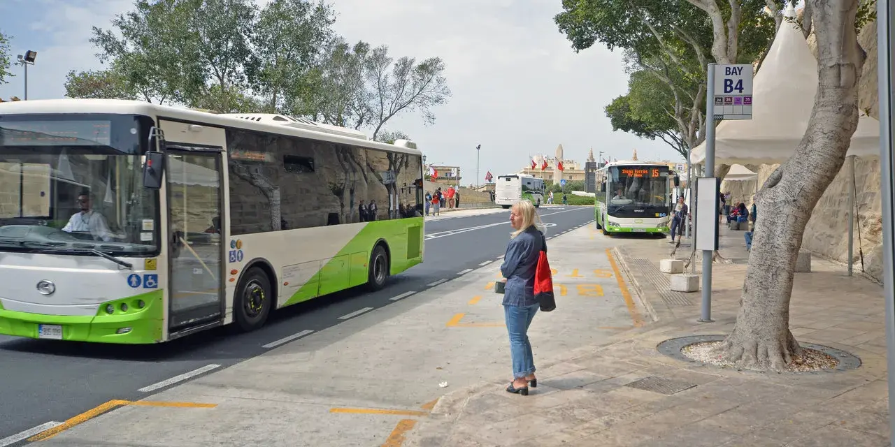 Kobieta czeka na autobus na Malcie. W tle widać autobusy, w tym jeden jadący w kierunku lotniska.
