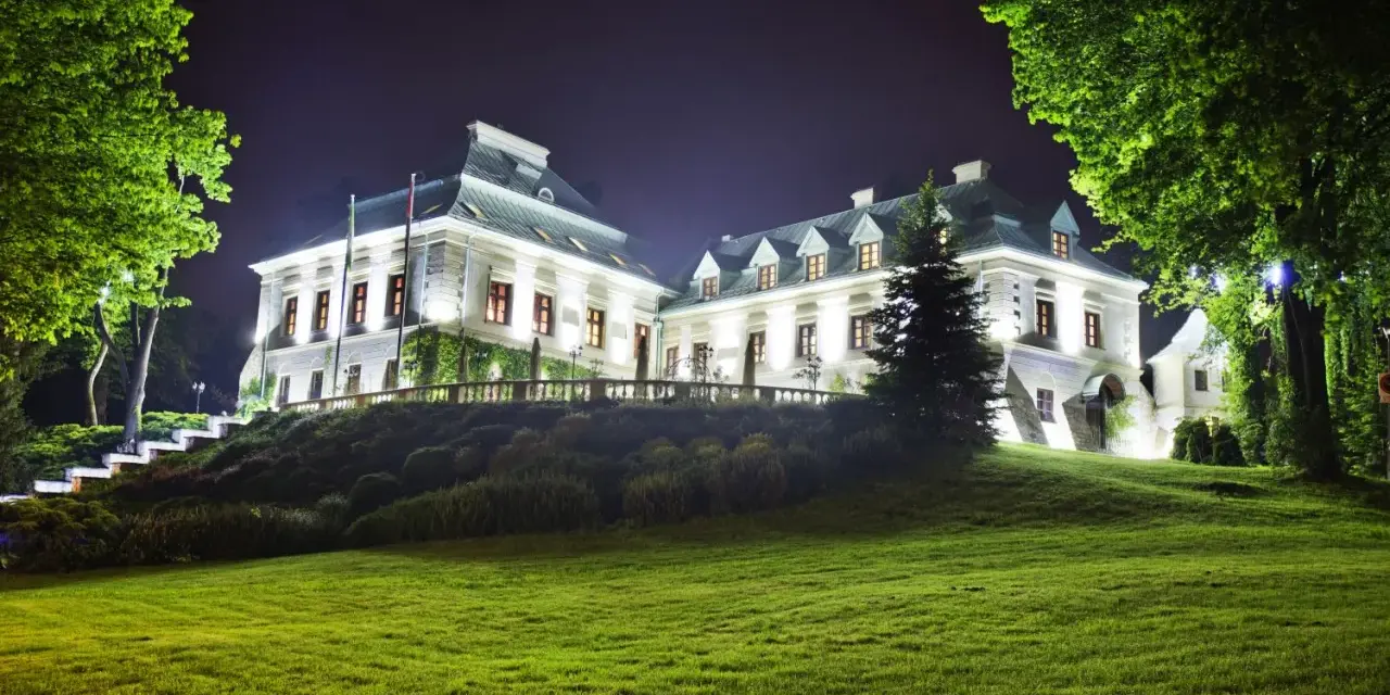 Elegancki hotel z atrakcjami dla dorosłych, nocą oświetlony, z pięknym ogrodem i zielonym trawnikiem.