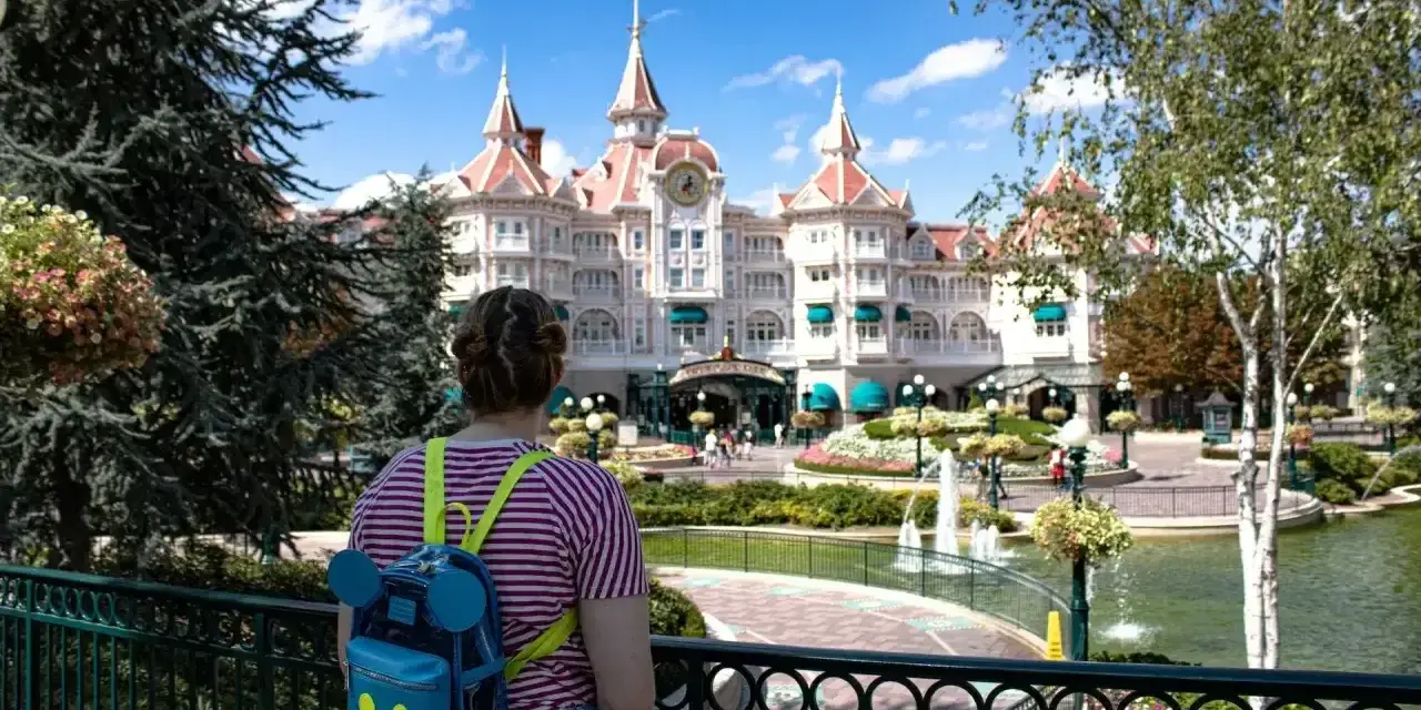 Dziewczyna z plecakiem w kształcie Myszki Miki podziwia zamek w Disneyland Paris. Bilety do parku już kupione, czas na przygodę!