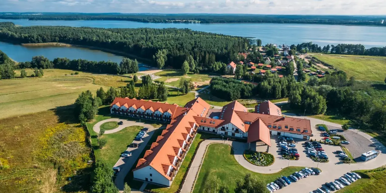 Malowniczy widok na Mikołajki Resort Spa z lotu ptaka, otoczony lasami i jeziorem. Idealne miejsce na relaks.