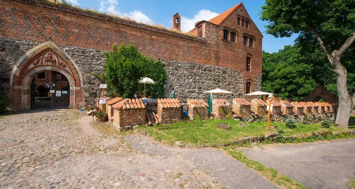 Kamienne mury i ceglane budynki tworzą malowniczy zamek bierzgłowski. Przed wejściem, na brukowanym dziedzińcu, stoją małe, urocze budowle z dachówkami.
